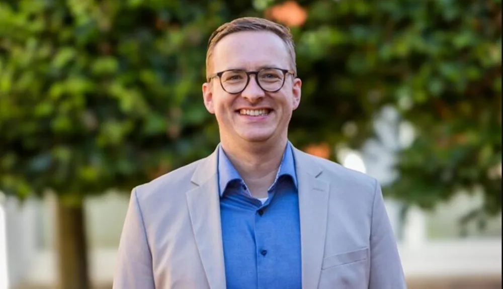 Porträt von Tobias Leschke mit Brille und beigem Sakko, lächelnd in die Kamera blickend.