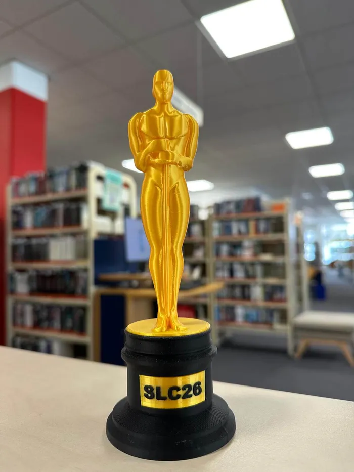Eine goldene Statue auf einem schwarzen Sockel mit der Aufschrift „SLC26“ in einer Bibliothek.
