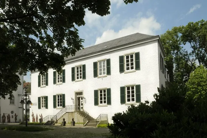 Weißes, zweistöckiges Gebäude der Stadtbücherei Letmathe mit grünen Fensterläden und einer Steintreppe zum Eingang.