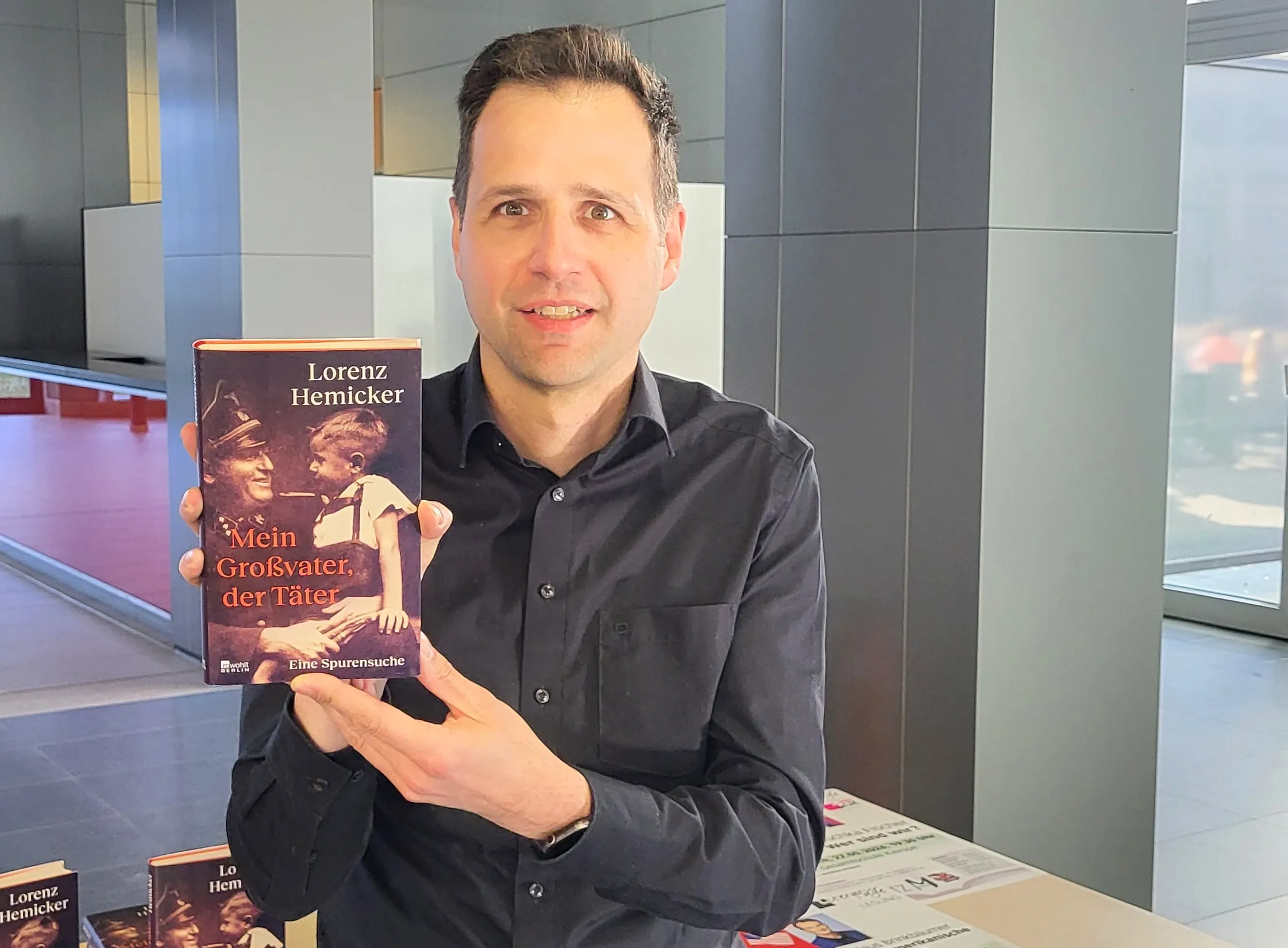 Lorenz Hemicker hält sein Buch „Mein Großvater, der Täter“ vor sich. Das Buch zeigt ein Schwarzweißfoto eines Mannes in Uniform und einen jüngeren Mann, der auf einem Motorrad sitzt.