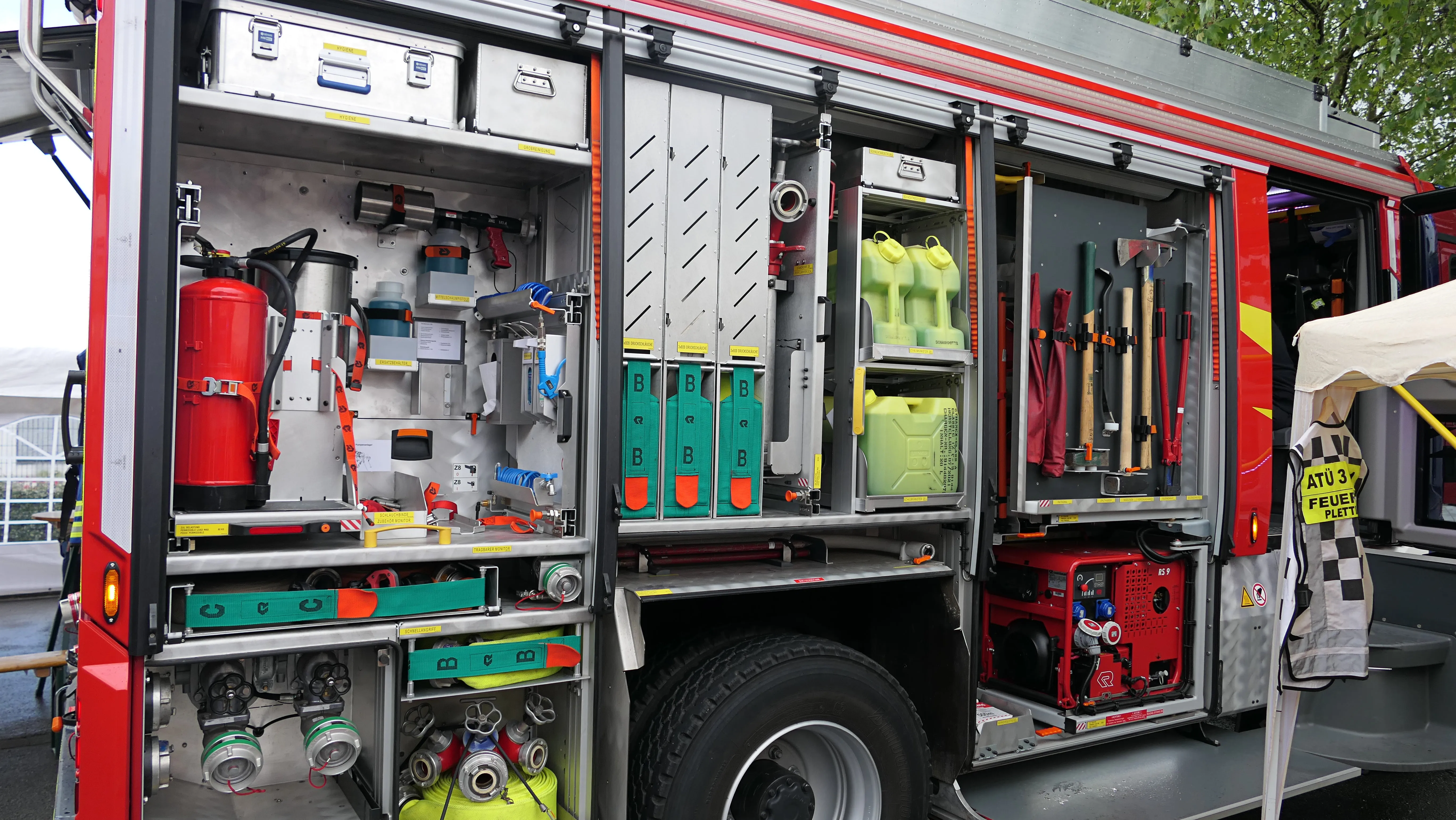 Offene Fächer eines roten Feuerwehrautos mit ausgestatteter Einsatzkleidung, Atemschutzgeräten und Werkzeugen.