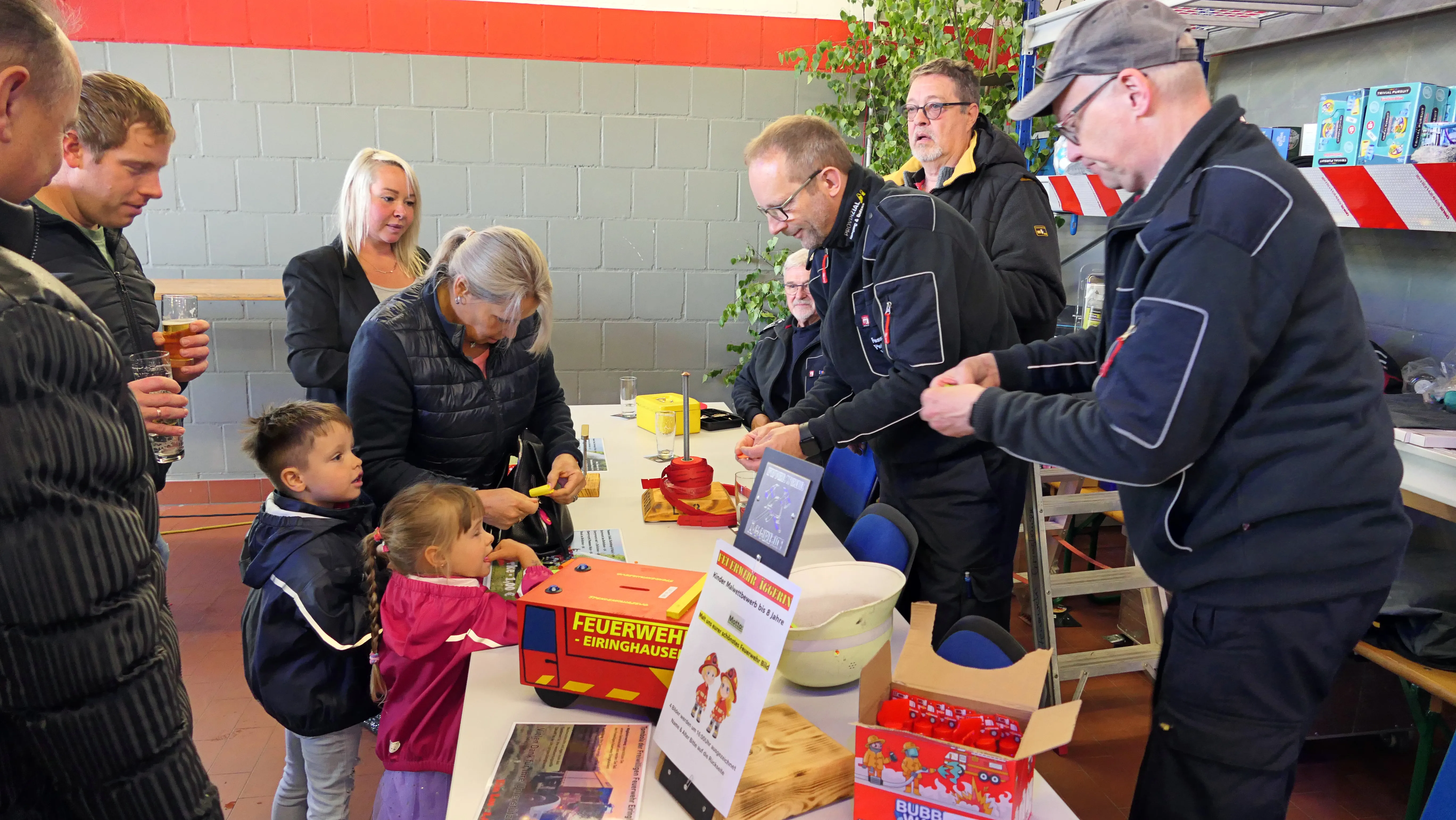 Feuerwehrleute erklären Kindern und Erwachsenen an einem Tisch die Funktionsweise eines Geräts, während andere Besucher im Hintergrund stehen und sich unterhalten.