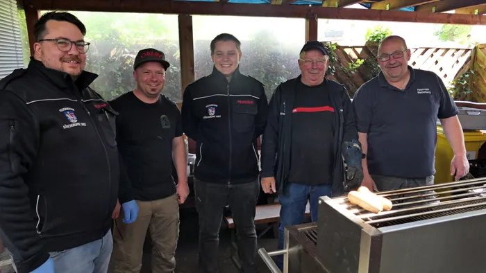Fünf Männer stehen lächelnd vor einem Grill im Freien. Sie tragen alle Jacken oder Poloshirts mit dem Aufdruck der Löschgruppe Ohle.