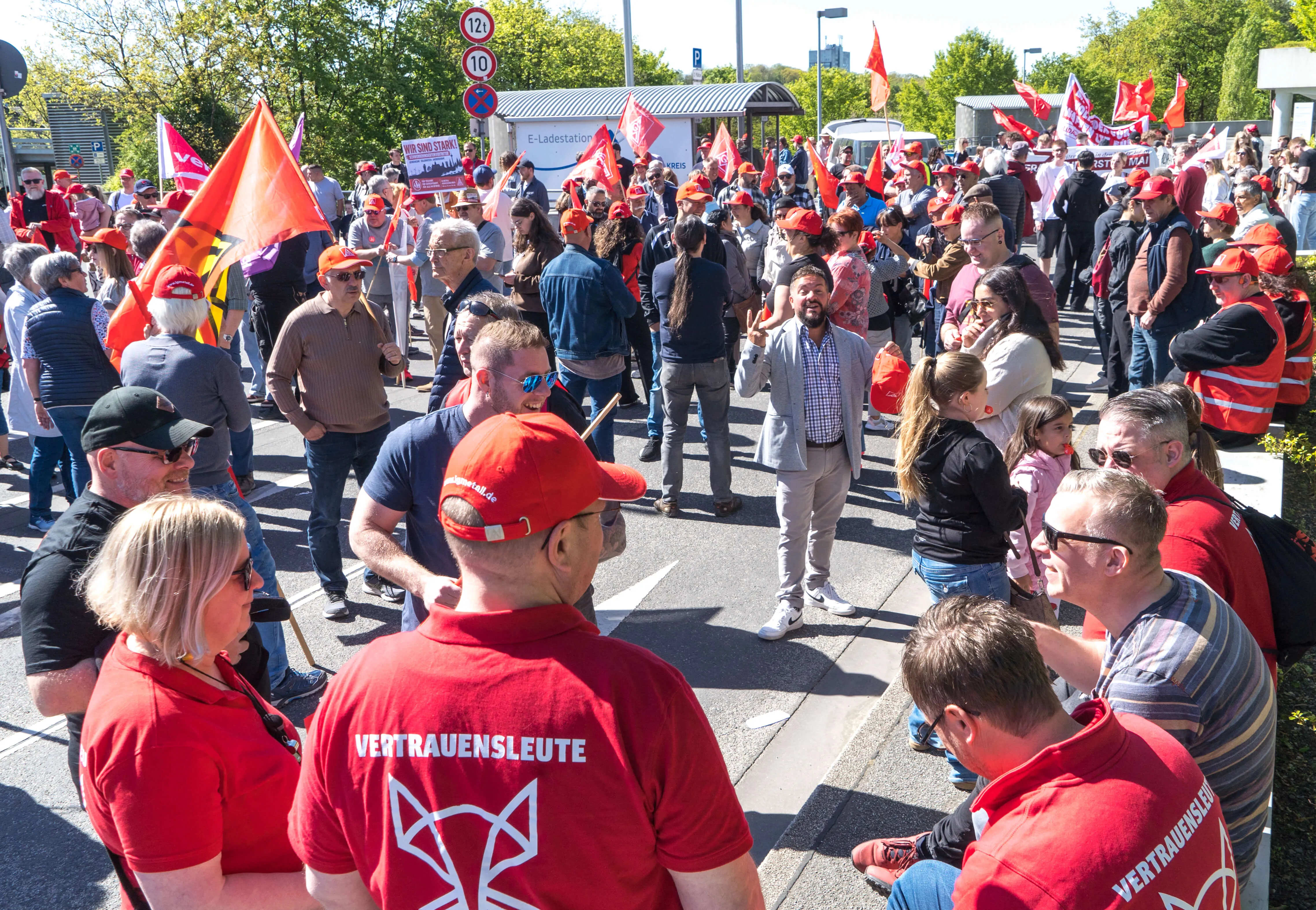 Große Menschenmenge bei einer Demonstration auf einem Platz vor einem Rathaus, viele tragen rote Kleidung und Schilder mit dem Aufdruck „VERTRAUENSLEUTE“ und einem Fuchs-Symbol.