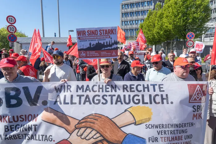 Demonstranten mit Transparenten und roten Mützen stehen vor dem Lüdenscheider Rathaus. Im Vordergrund ein Banner mit der Aufschrift „Wir machen Rechte Alltagstauglich“ und zwei Händen, die sich halten.