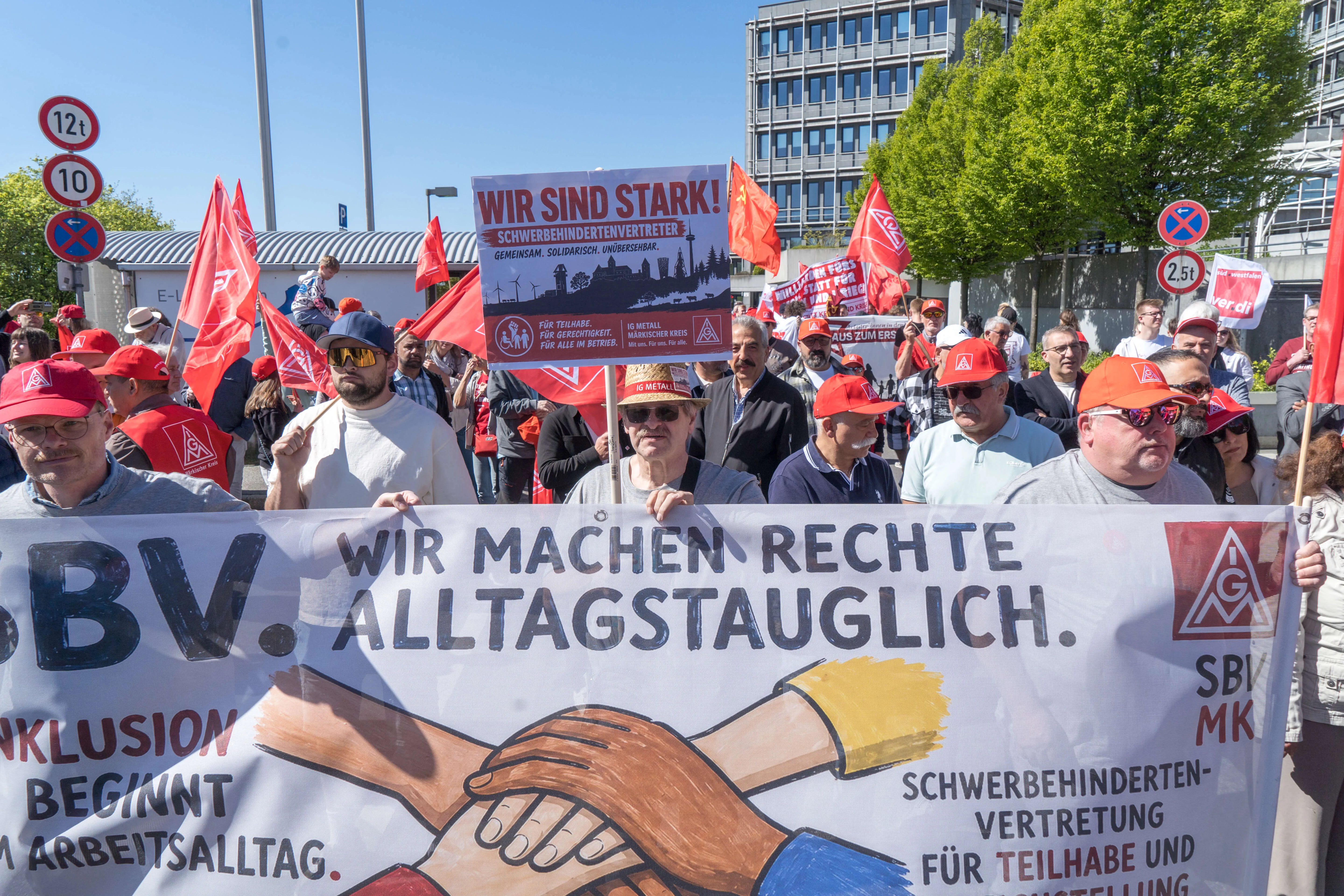 Demonstranten mit Transparenten und roten Mützen stehen vor dem Lüdenscheider Rathaus. Im Vordergrund ein Banner mit der Aufschrift „Wir machen Rechte Alltagstauglich“ und zwei Händen, die sich halten.