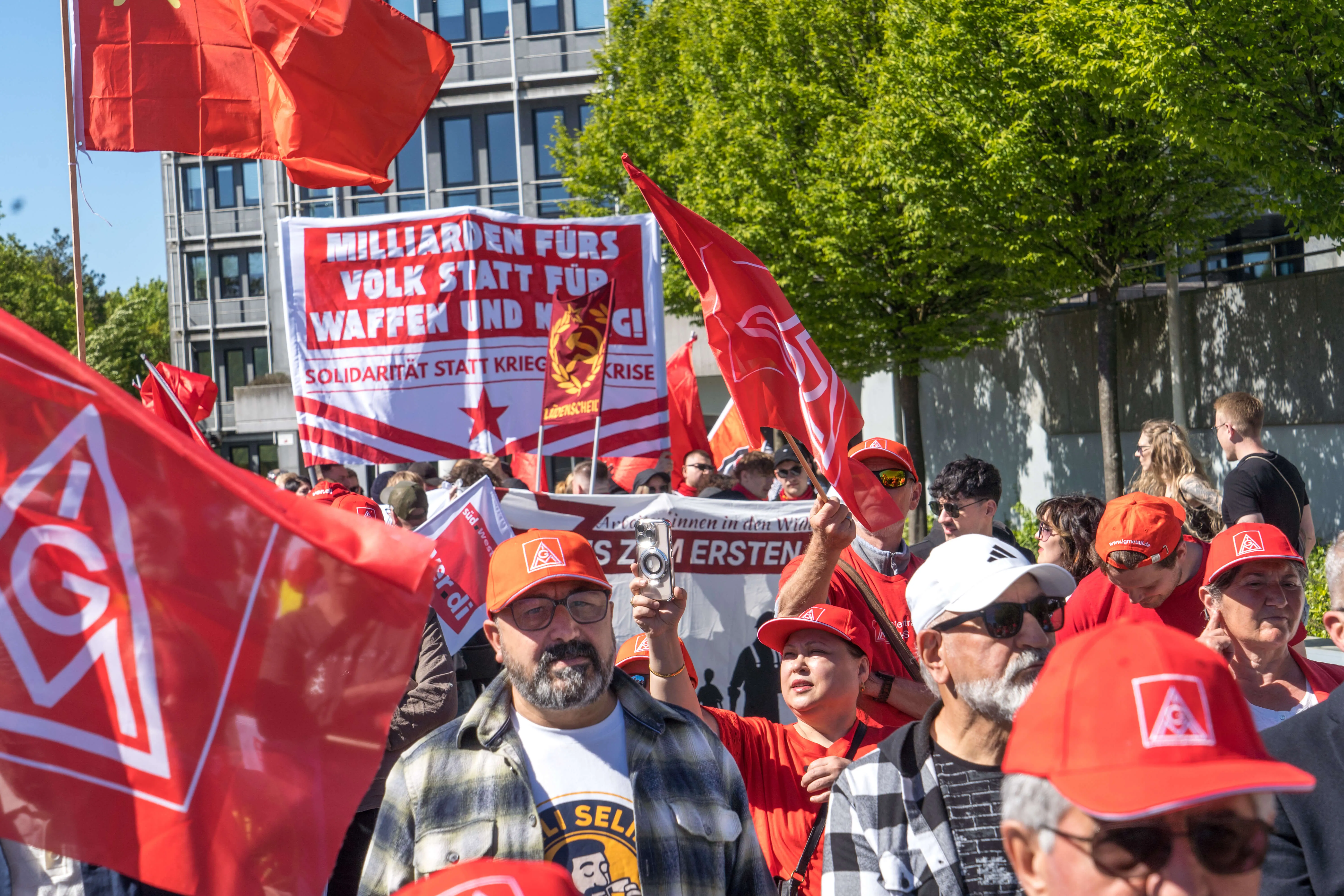 Demonstranten halten rote Fahnen und Transparente mit der Aufschrift „Milliarden fürs Volk statt für Waffen und Krieg – Solidarität statt Krise“ auf dem Lüdenscheider Rathausplatz.
