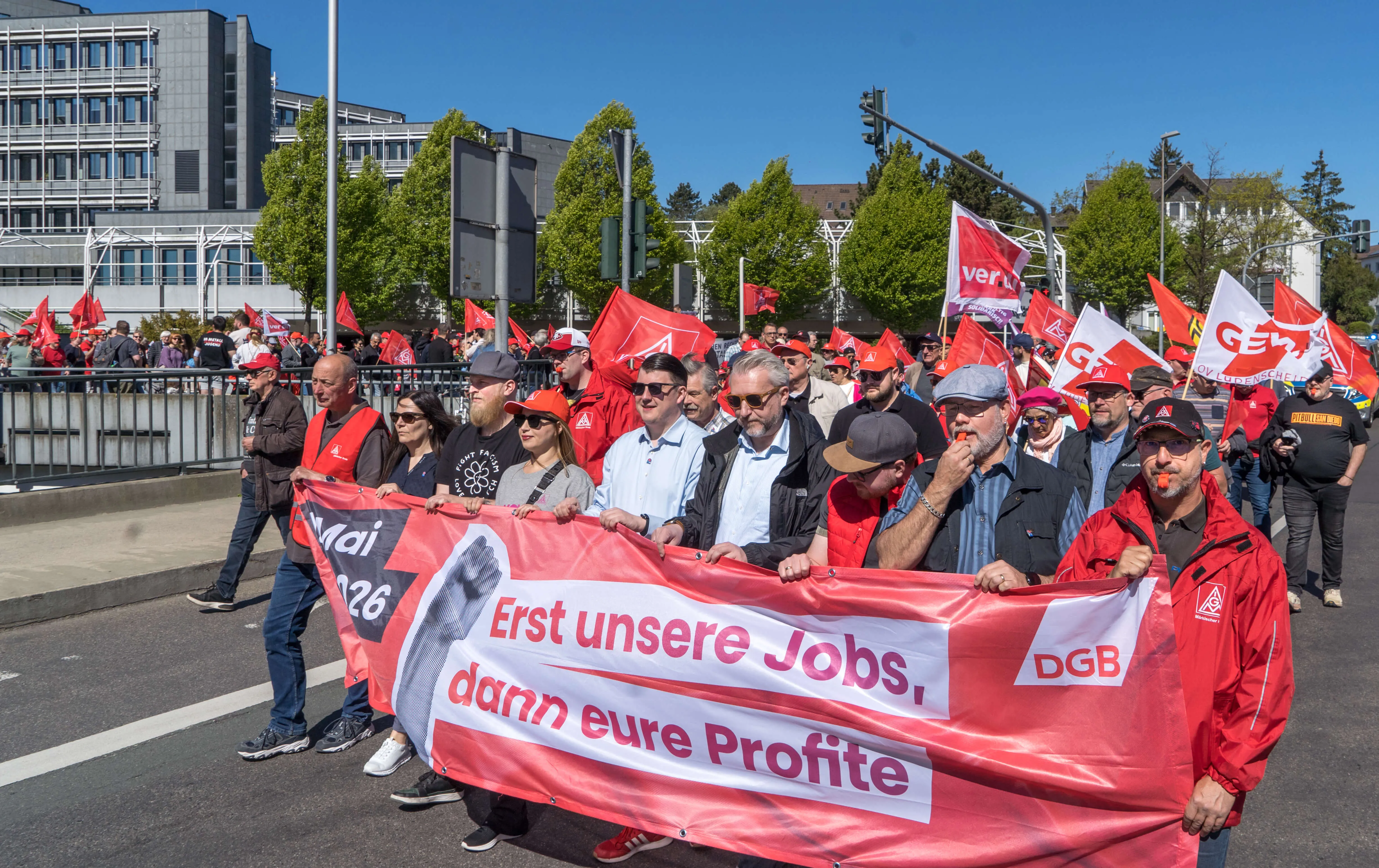 Demonstranten tragen ein Banner mit der Aufschrift „Erst unsere Jobs, dann eure Profite“ bei einer Mai-Kundgebung auf dem Lüdenscheider Rathausplatz.
