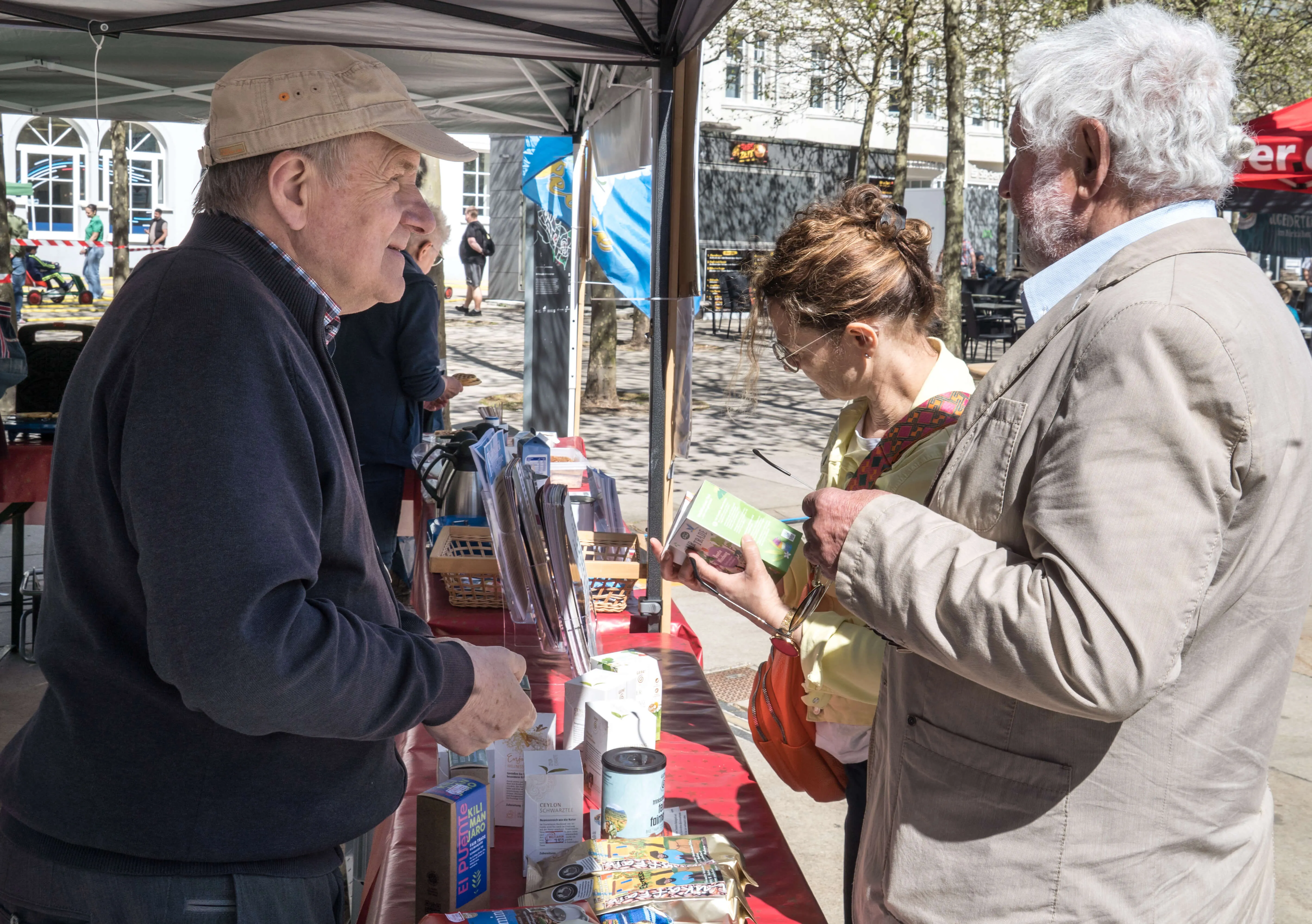 Zwei ältere Männer und eine Frau betrachten Bücher und andere Artikel an einem Marktstand auf dem Lüdenscheider Rathausplatz.