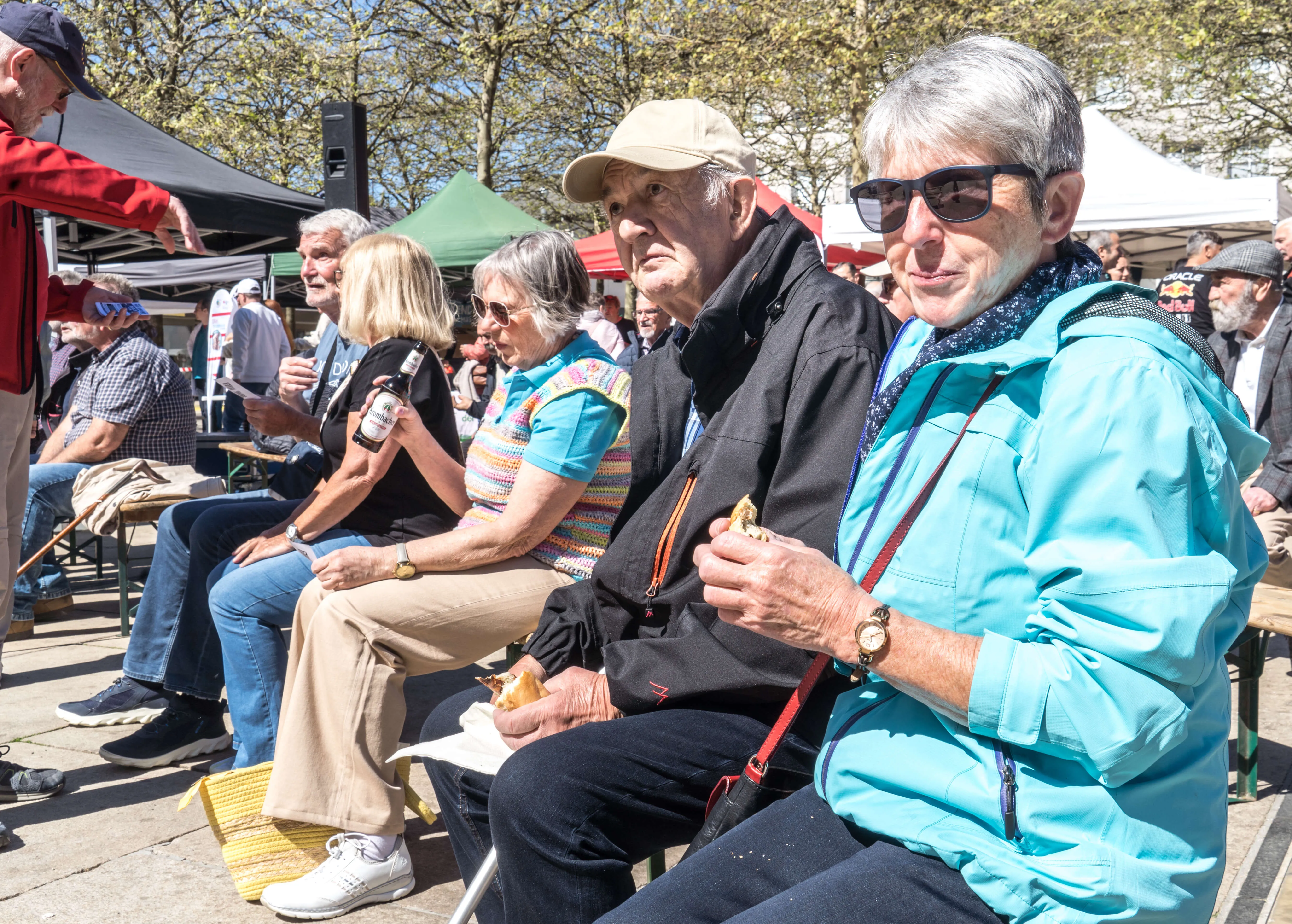 Mehrere Menschen sitzen auf Bänken und essen Würstchen während einer Veranstaltung auf dem Lüdenscheider Rathausplatz.