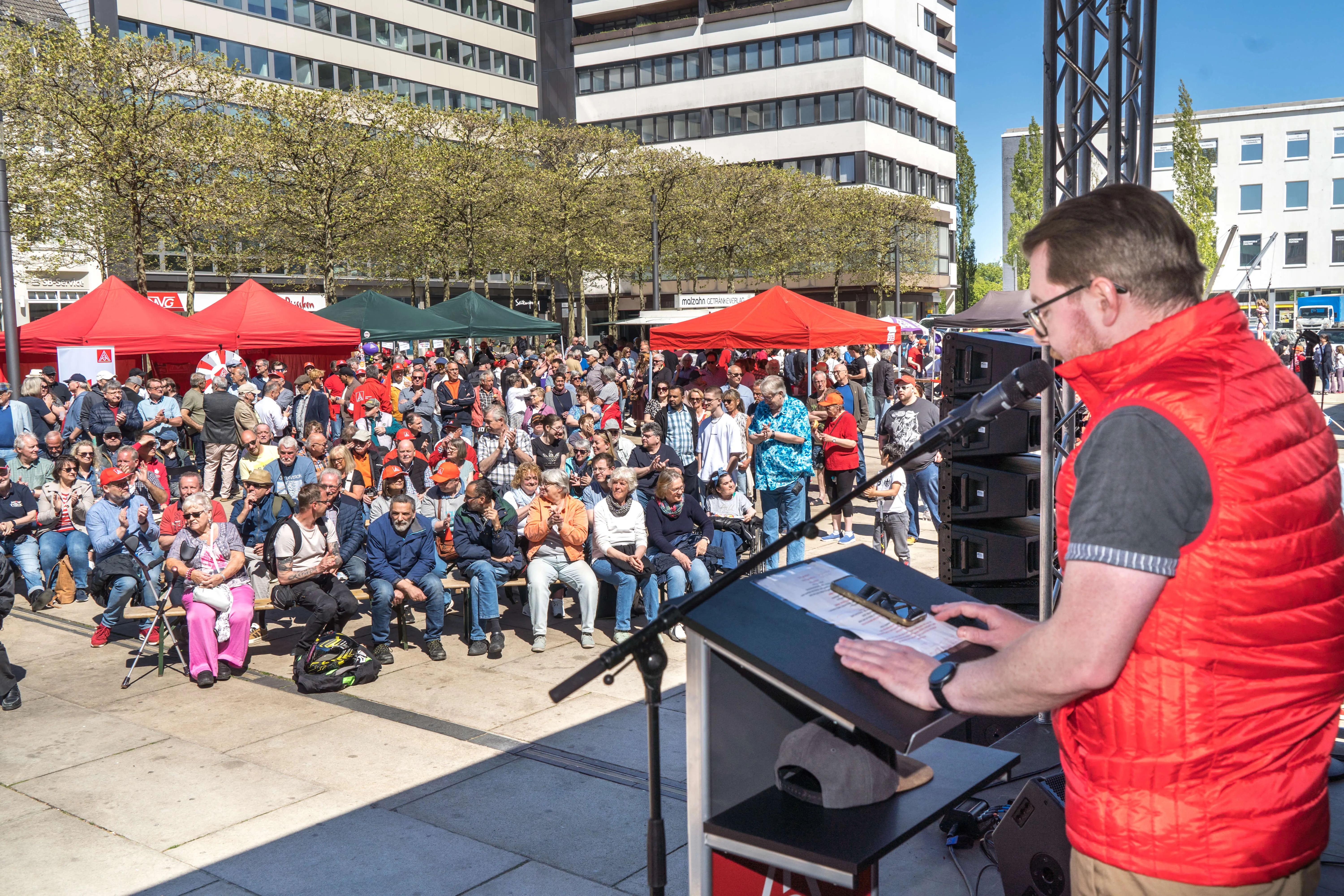Mann mit roter Weste spricht auf einer Kundgebung vor einer großen Menschenmenge auf dem Lüdenscheider Rathausplatz.