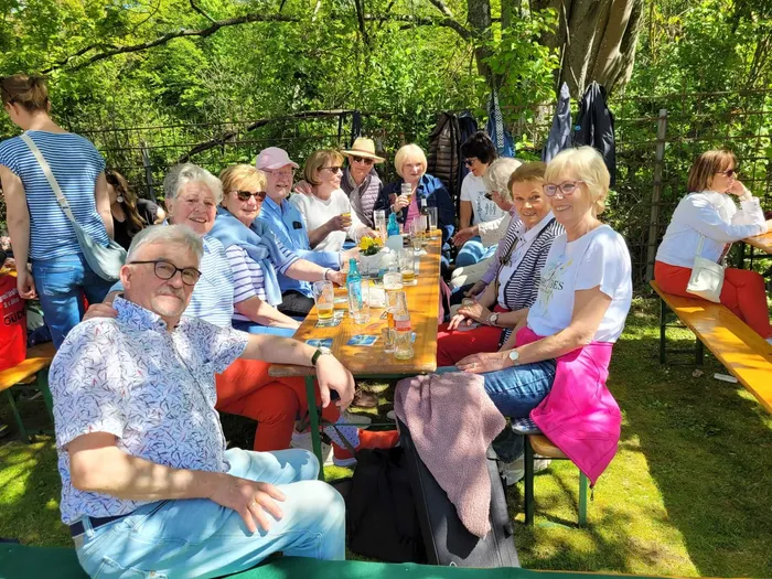 Eine Gruppe von Menschen sitzt an Biertischgarnituren im Freien, umgeben von Grün und Bäumen. Sie unterhalten sich, trinken und genießen die Maifeier des SGV Eiringhausen.