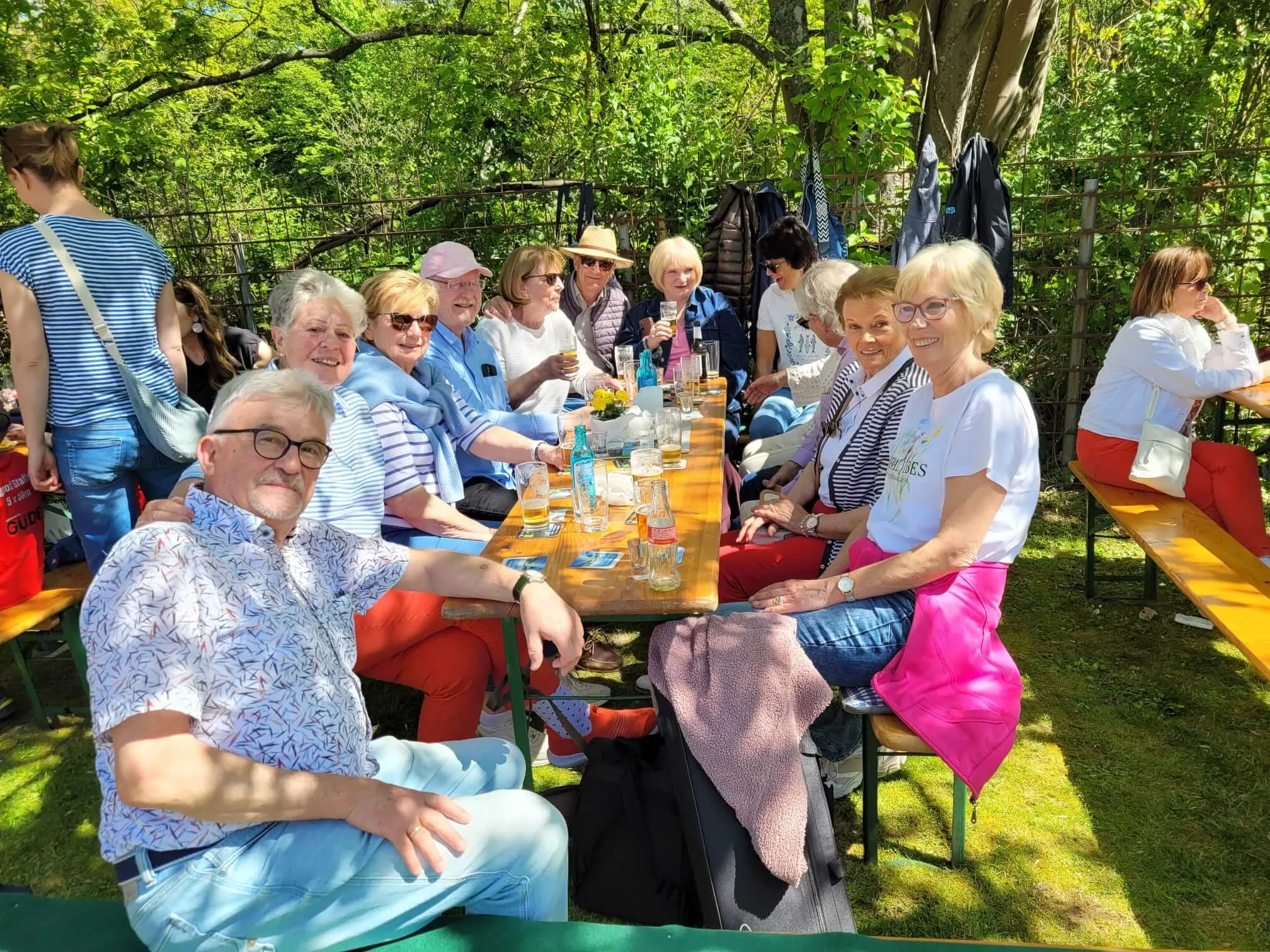 Eine Gruppe von Menschen sitzt an Biertischgarnituren im Freien, umgeben von Grün und Bäumen. Sie unterhalten sich, trinken und genießen die Maifeier des SGV Eiringhausen.