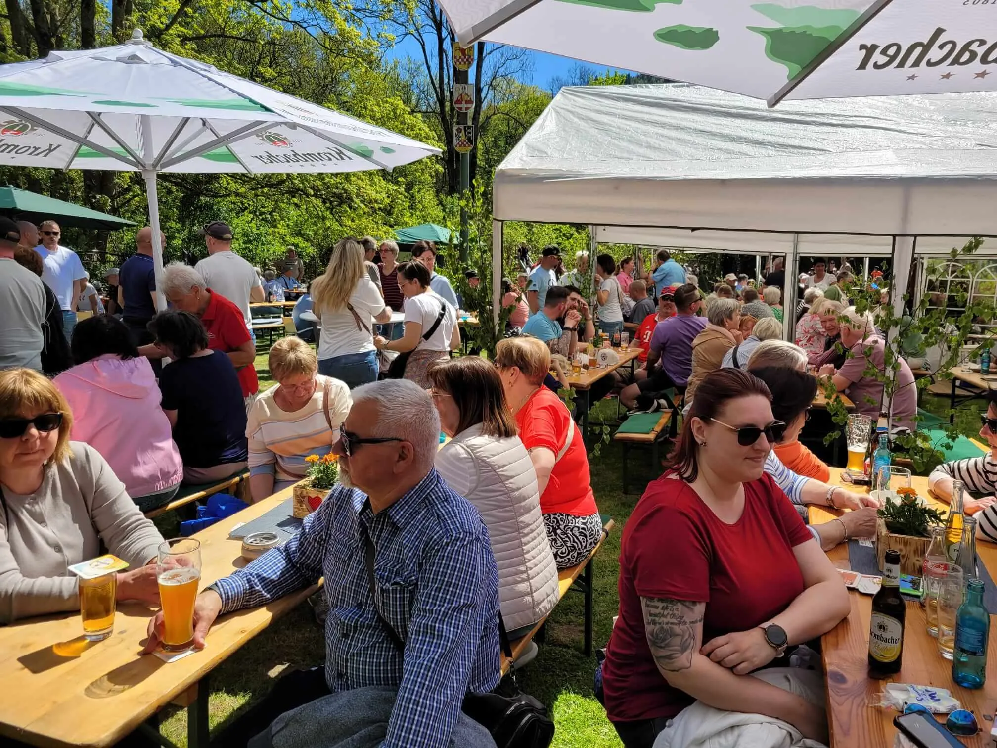 Menschen sitzen an Biertischen unter Sonnenschirmen und genießen ein Frühlingsfest im Freien.