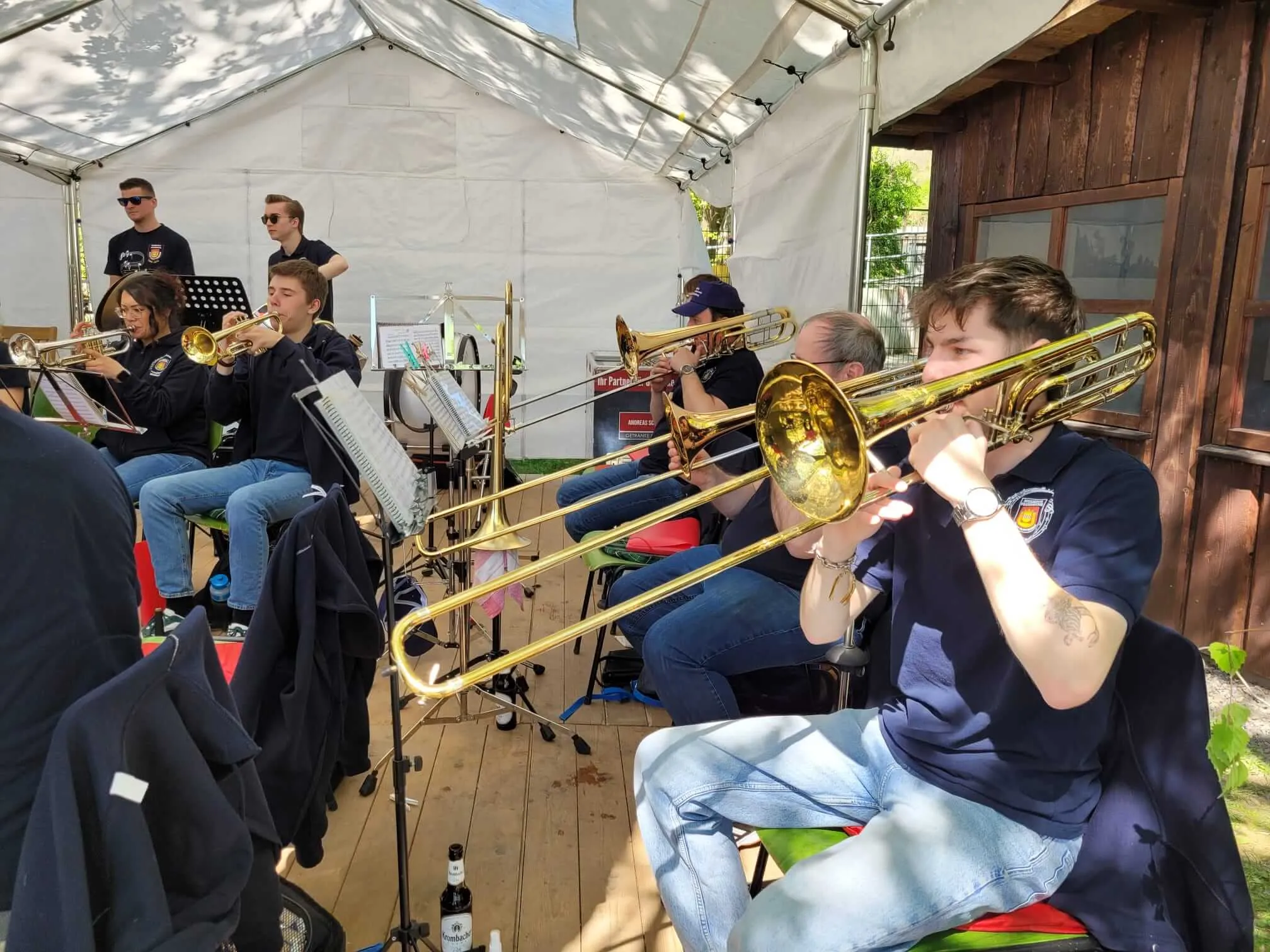 Mehrere Musiker spielen Posaunen und andere Blechblasinstrumente unter einem Zelt während einer Maifeier des SGV Eiringhausen.