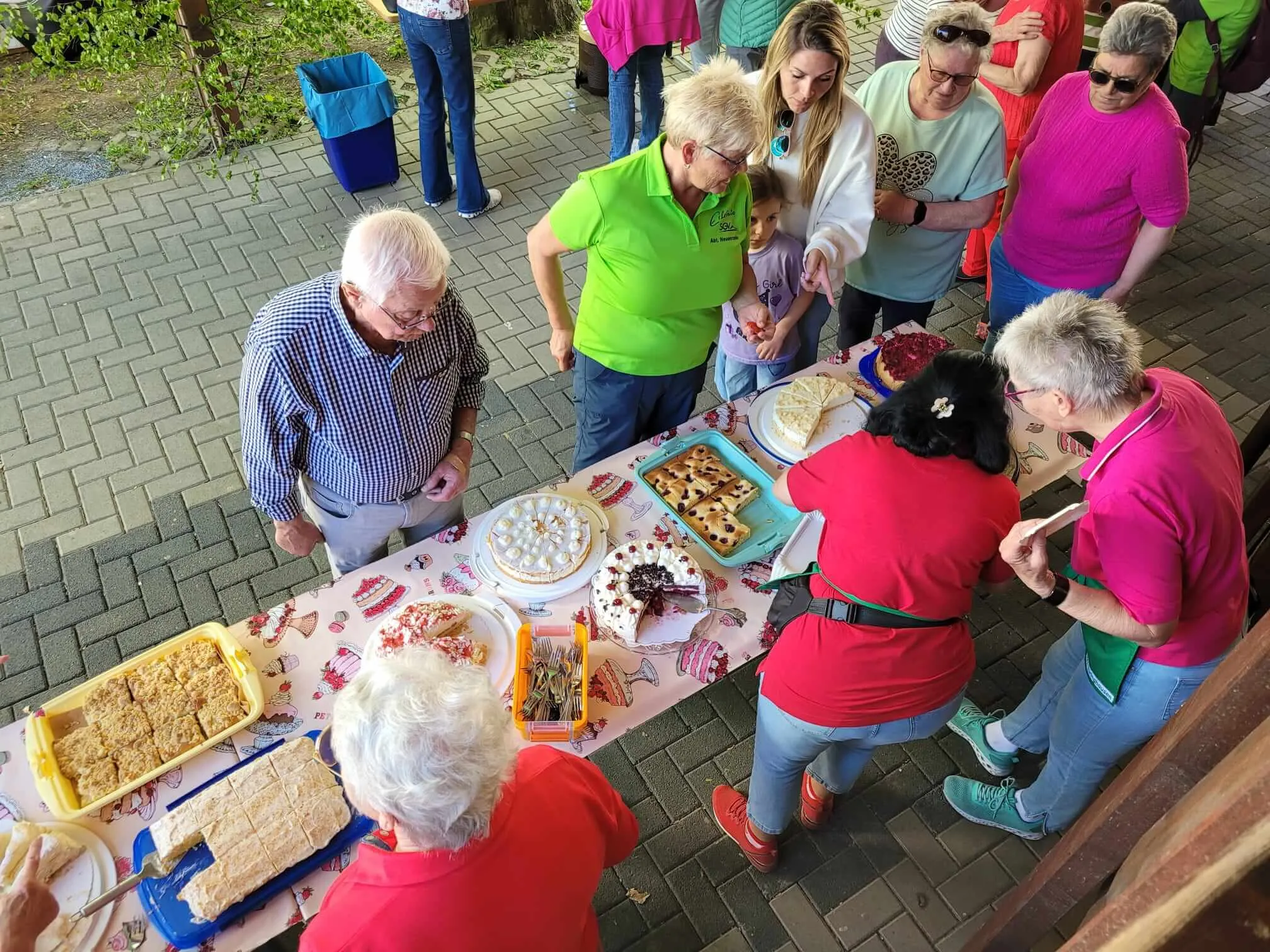 Menschen stehen um einen Tisch mit Kuchen und Gebäck im Freien. Im Hintergrund weitere Besucher der Maifeier des SGV Eiringhausen.