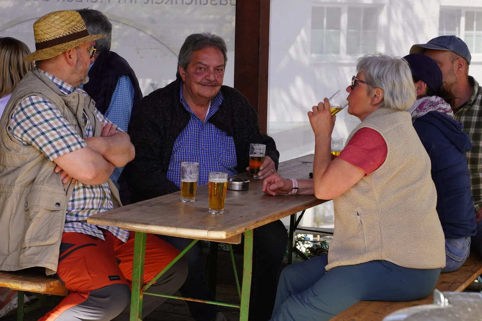 Eine Gruppe von Menschen sitzt an einem Biergartentisch und unterhält sich bei Getränken im Freien.