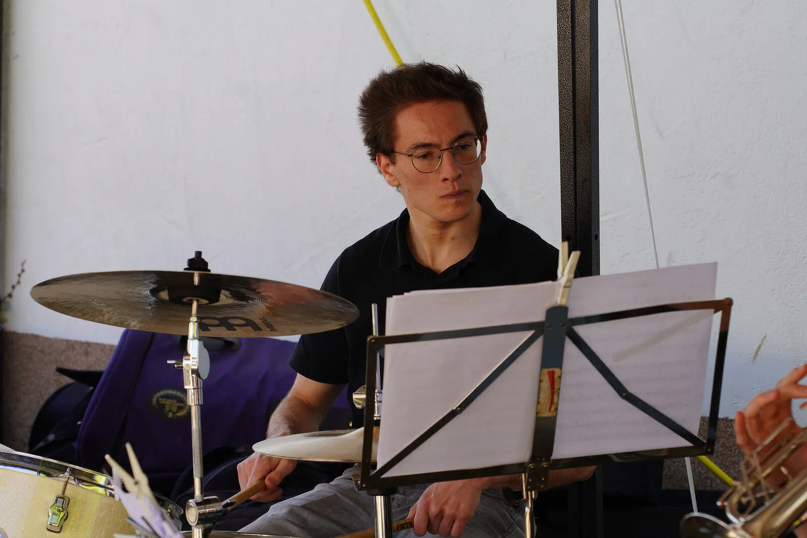 Ein junger Schlagzeuger mit Brille spielt auf einem Maifruhschoppen im Freien, vor ihm ein Notenständer mit Musikblättern.