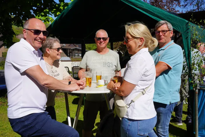 Mehrere Menschen stehen und unterhalten sich an einem Tisch mit Getränken unter einem Pavillon während eines Frühlingsfestes.