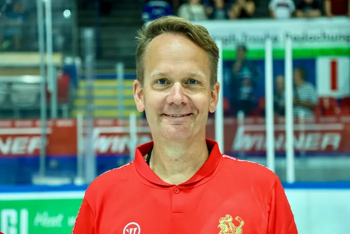 Dr. Jochen Veit, Mannschaftsarzt der Iserlohn Roosters, lächelt in einem Porträt vor dem Hintergrund einer Eishalle.