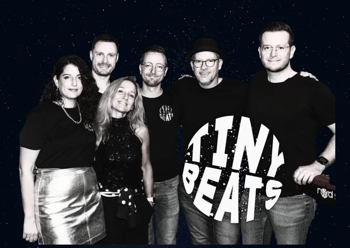 Sechs Mitglieder der Musikgruppe „Tiny Beats“ posieren vor einem dunklen, punktierten Hintergrund.
