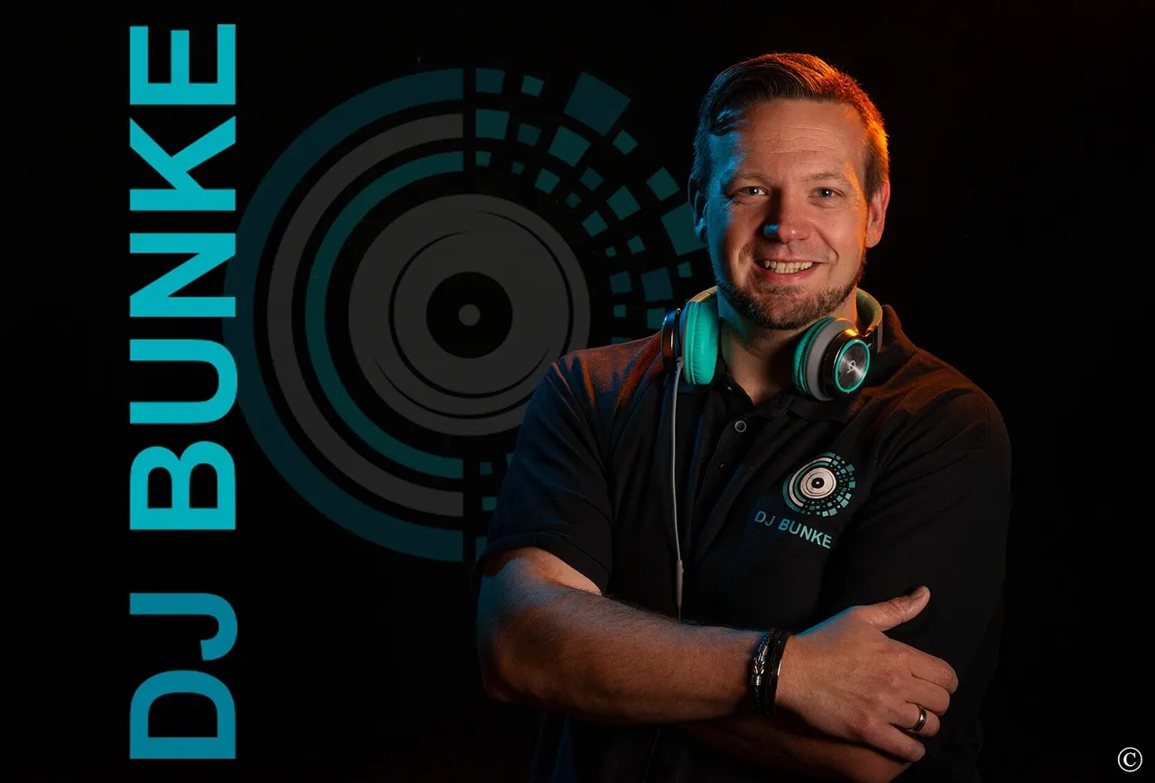 DJ Bunke lächelt mit verschränkten Armen und trägt türkisfarbene Kopfhörer um den Hals.