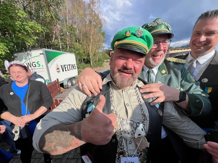 Ein lächelnder Mann mit grünem Hut und großer Kette gibt einen Daumen hoch, umgeben von Männern in grünen Uniformen beim Kreiskönigsschießen 2026.