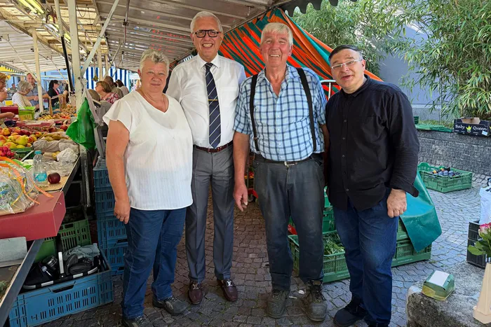 Vier Personen stehen auf einem Markt vor einem Obststand. Bürgermeister Ralf Beßler und Ordnungsamtsleiter Thorsten Spiegel gratulieren Heide und Günter Deitelhoff zu ihrem Ruhestand.