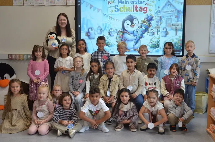 Klassenlehrerin Johanna Voit mit ihrer Pinguin-Klasse vor einem Bildschirm mit der Aufschrift „Mein erster Schultag“.