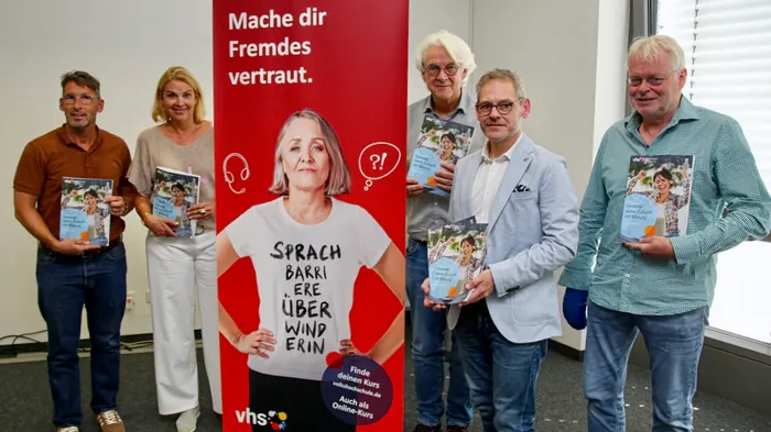Fünf Personen halten Broschüren des neuen Jahresprogramms der VHS Iserlohn vor einem großen roten Roll-up-Banner.