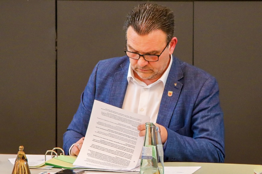Bürgermeister Michael Joithe liest während einer Veranstaltung konzentriert ein Dokument. Vor ihm steht eine Flasche Wasser.