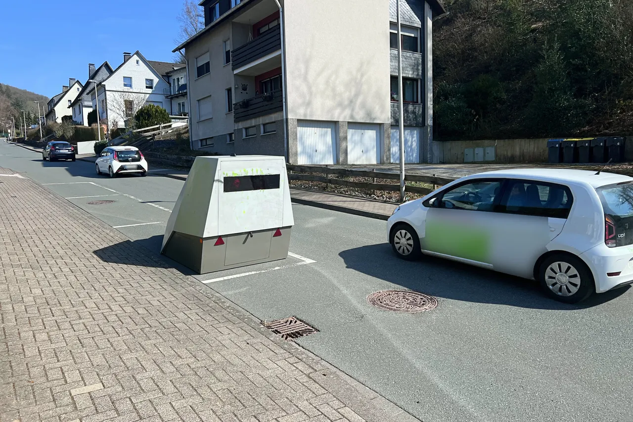 Mobiler Blitzer steht am Straßenrand einer Wohngegend in Plettenberg, Nordrhein-Westfalen. Im Hintergrund sind geparkte Autos und Wohnhäuser zu sehen.