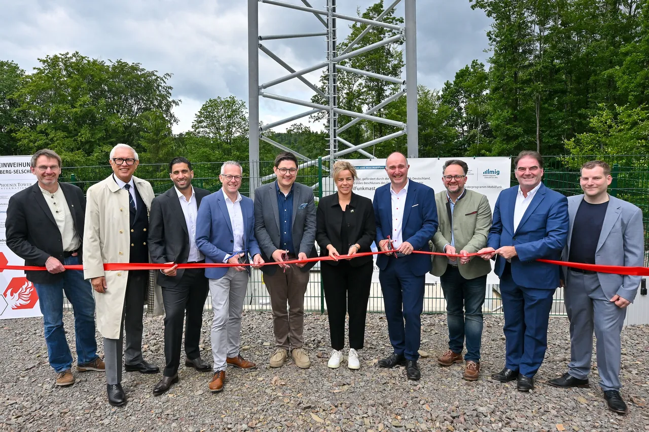 Gruppe von Männern und einer Frau schneidet ein rotes Band vor einem hohen Metallfunkmast durch. Die Gruppe besteht aus Politikern und Vertretern von Telekommunikationsunternehmen.
