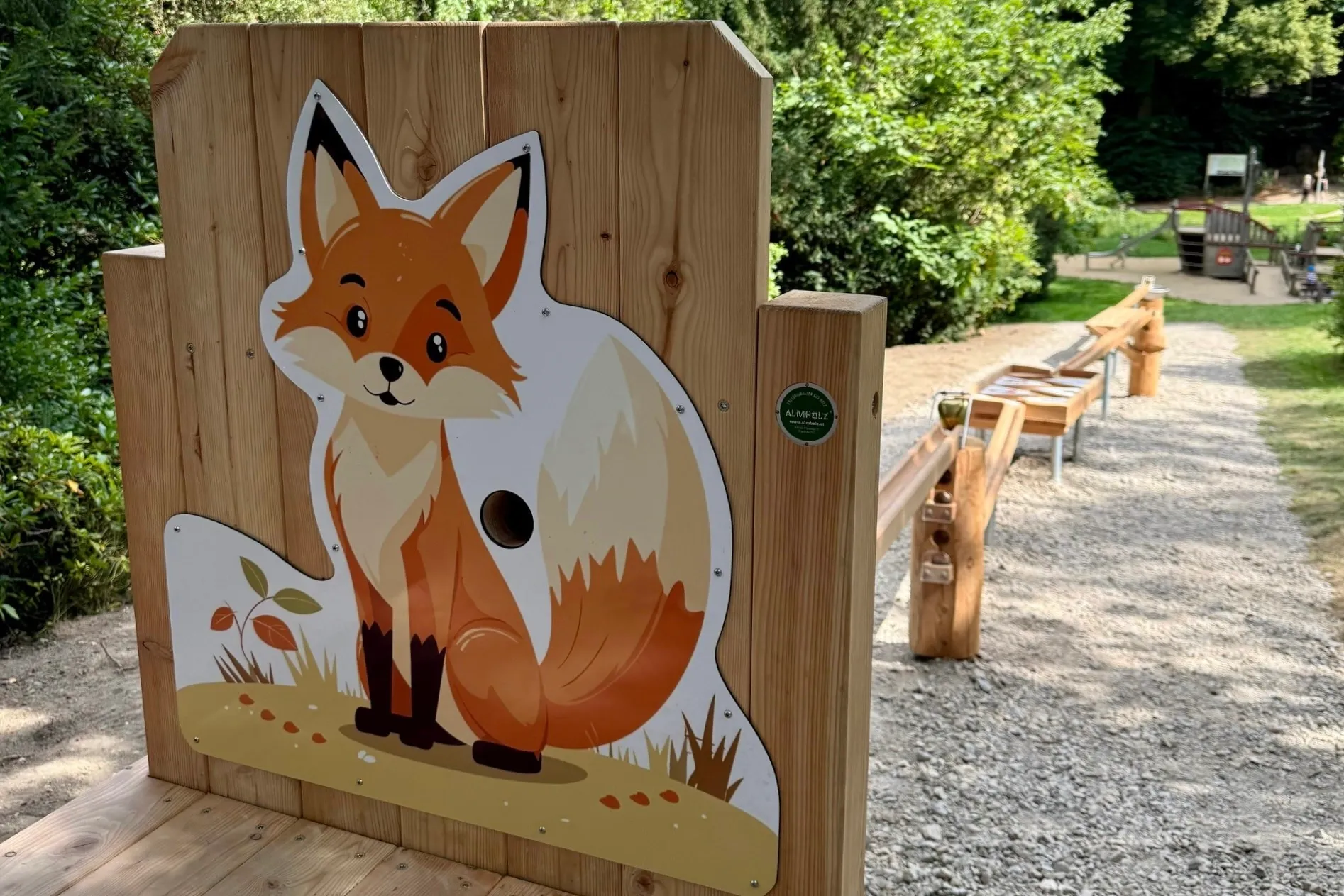 Holzkonstruktion mit einem Fuchs-Motiv und mehreren Löchern für Murmeln, Teil einer Outdoor-Murmelbahn.