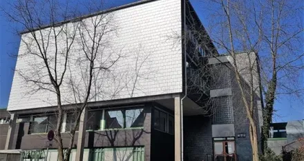 Das Gebäude der Musikschule Volmetal in Halver zeigt eine moderne Fassade mit hellen und dunklen Elementen. Mehrere Fenster und ein dunkler Eingangsbereich sind erkennbar.
