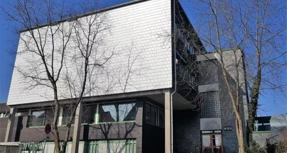 Das Gebäude der Musikschule Volmetal in Halver zeigt eine moderne Fassade mit hellen und dunklen Elementen. Mehrere Fenster und ein dunkler Eingangsbereich sind erkennbar.