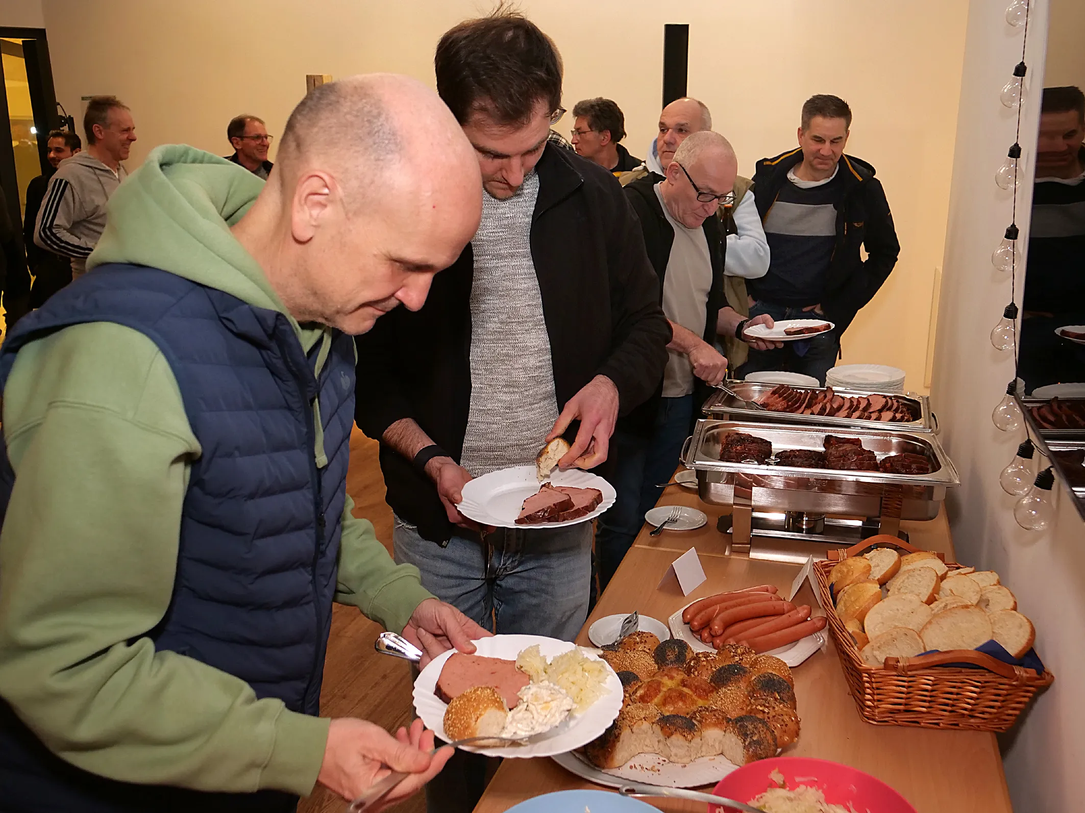 Männer bedienen sich an einem Buffet mit Fleisch, Wurst, Brot und Salaten während eines Abends in der Freikirchlichen Gemeinde Wiesenthal.