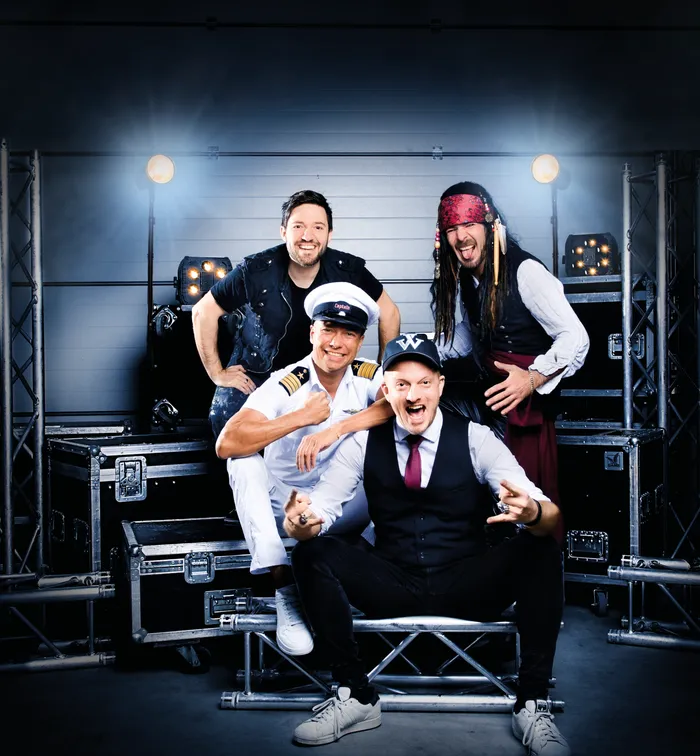 Die vier Mitglieder der Band Hitfluencer posieren in einem Studio vor Bühnenequipment und Scheinwerfern.