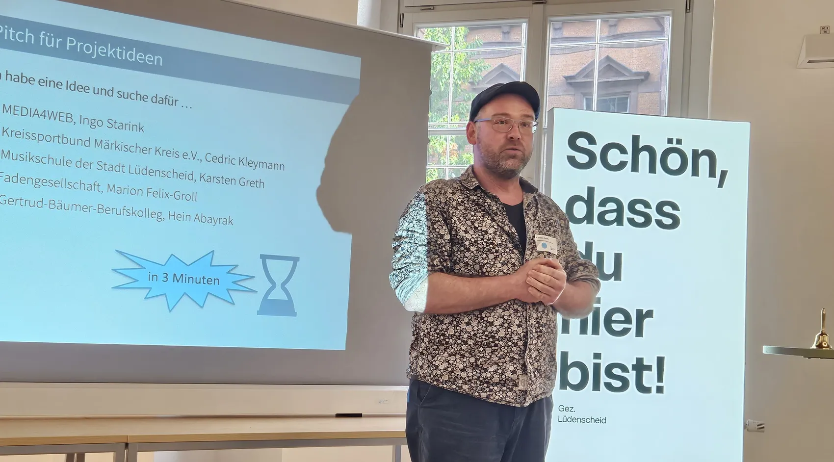 Karsten Greth steht vor einer Projektpräsentation und einem Schild mit der Aufschrift „Schön, dass du hier bist!“.