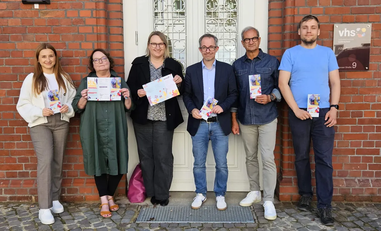Sechs Personen stehen vor einem Backsteingebäude der VHS und halten Flyer für eine Netzwerkveranstaltung in die Kamera.