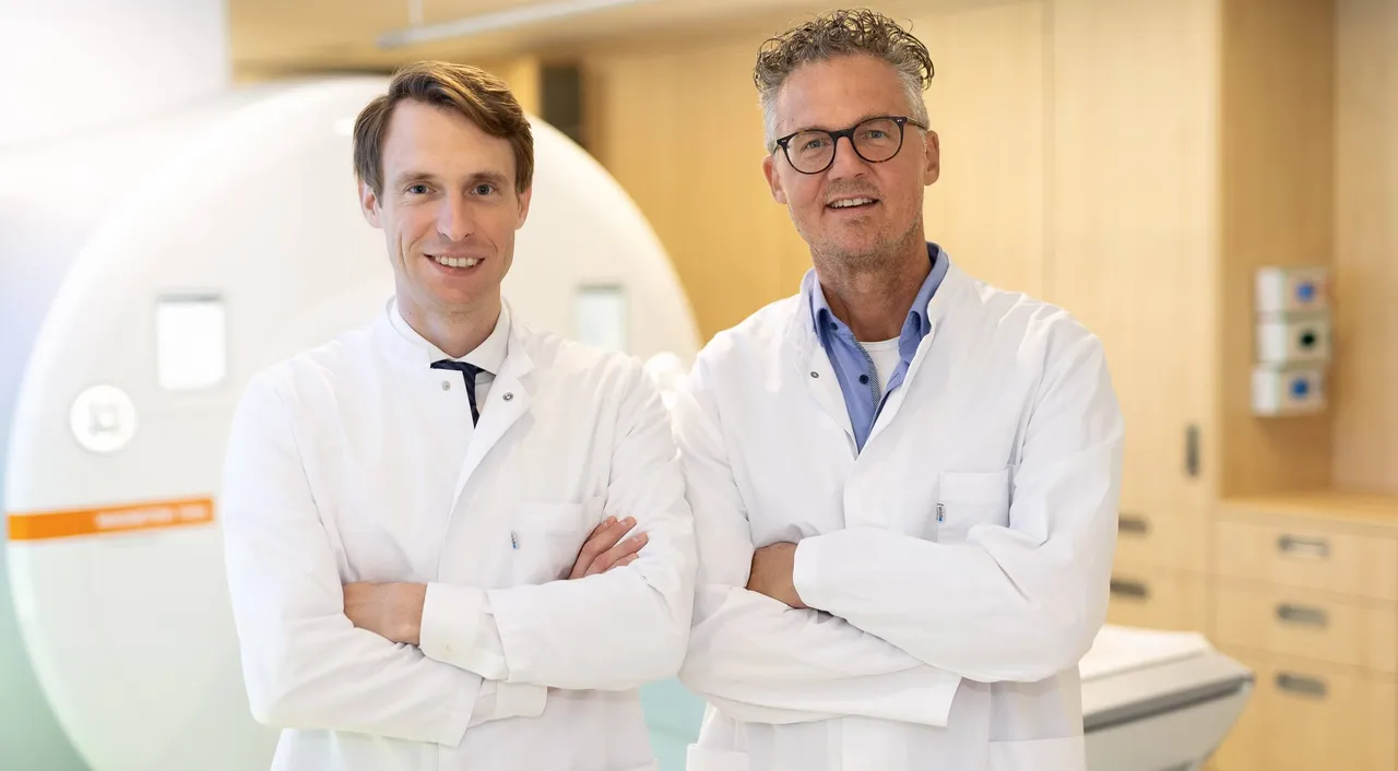 Dr. Thomas Alexander Ochtrop und Dr. Felix Kämmerer in weißen Arztkitteln stehen lächelnd mit verschränkten Armen vor einem medizinischen Scanner.