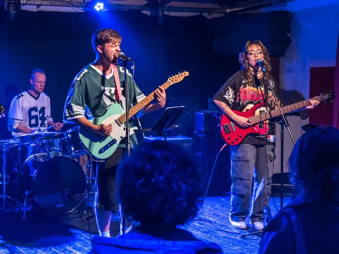 Die Band „Not4Me“ tritt live auf einer Bühne auf, wobei ein Gitarrist und eine Bassistin singend ihre Instrumente spielen.