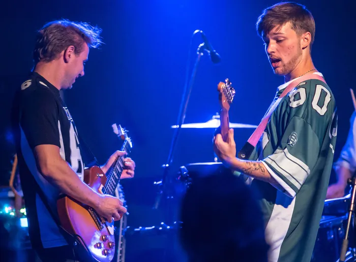 Zwei Musiker spielen E-Gitarren auf einer Bühne unter blauem Scheinwerferlicht bei einem Benefizkonzert.