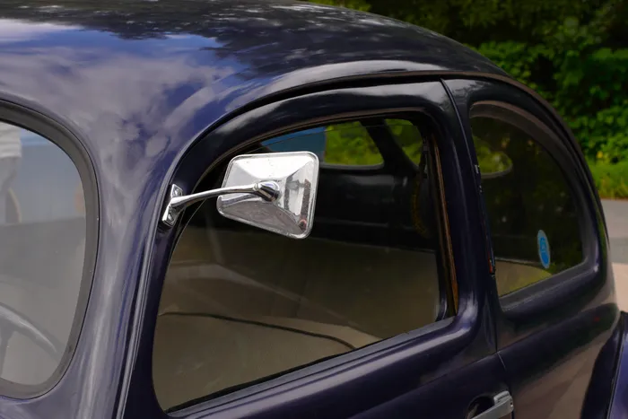 Nahaufnahme eines verchromten Außenspiegels an einem dunkelblauen Oldtimer.