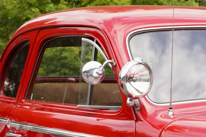 Detailaufnahme eines roten Oldtimers mit glänzenden Chrom-Spiegeln und einem runden Scheinwerfer.
