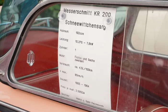 Ein Informationsblatt mit technischen Daten zum Messerschmitt KR 200 „Schneewittchensarg“ an der Windschutzscheibe eines roten Fahrzeugs.