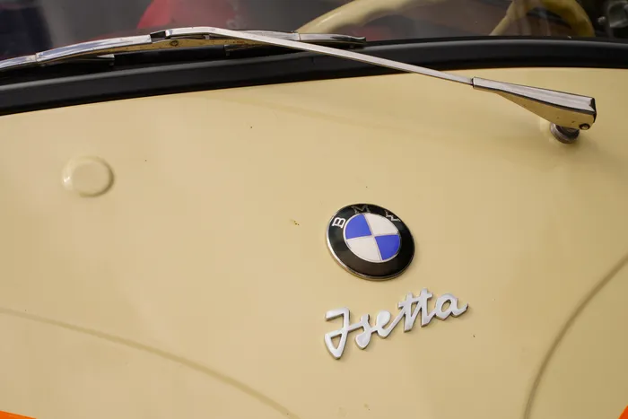 BMW-Emblem und der verchromte Schriftzug „Isetta“ auf der cremefarbenen Karosserie eines Oldtimers.