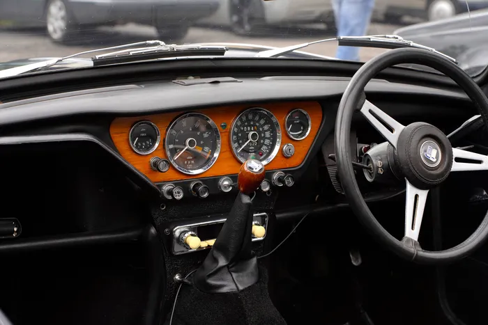Innenansicht des Armaturenbretts eines Triumph Speedfire von 1970 mit Holzdekor, analogen Instrumenten und schwarzem Lenkrad.