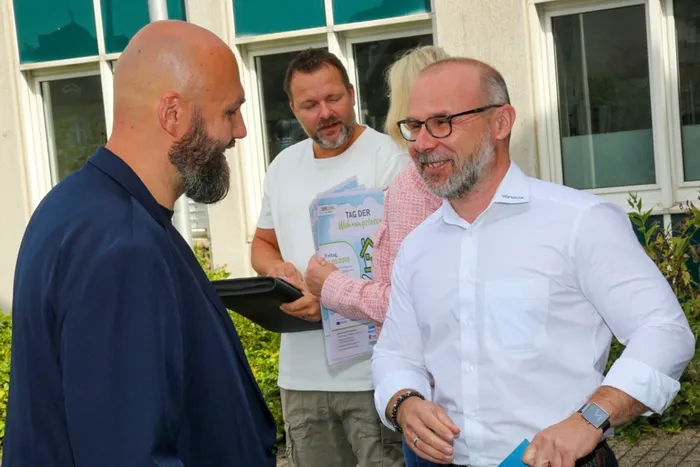 Oliver Funke und Karl Cielontko im Gespräch, während ein Mann im Hintergrund einen Flyer hält.