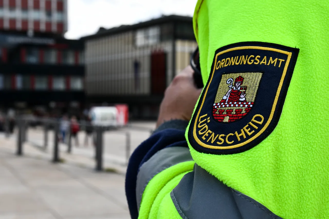 Ein Mitarbeiter des Ordnungsamtes Lüdenscheid mit einer fluoreszierenden Weste und einem Abzeichen auf dem Rücken ist zu sehen. Das Abzeichen zeigt das Stadtwappen und den Schriftzug 